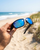man holding sunglasses showing while walking on the beach