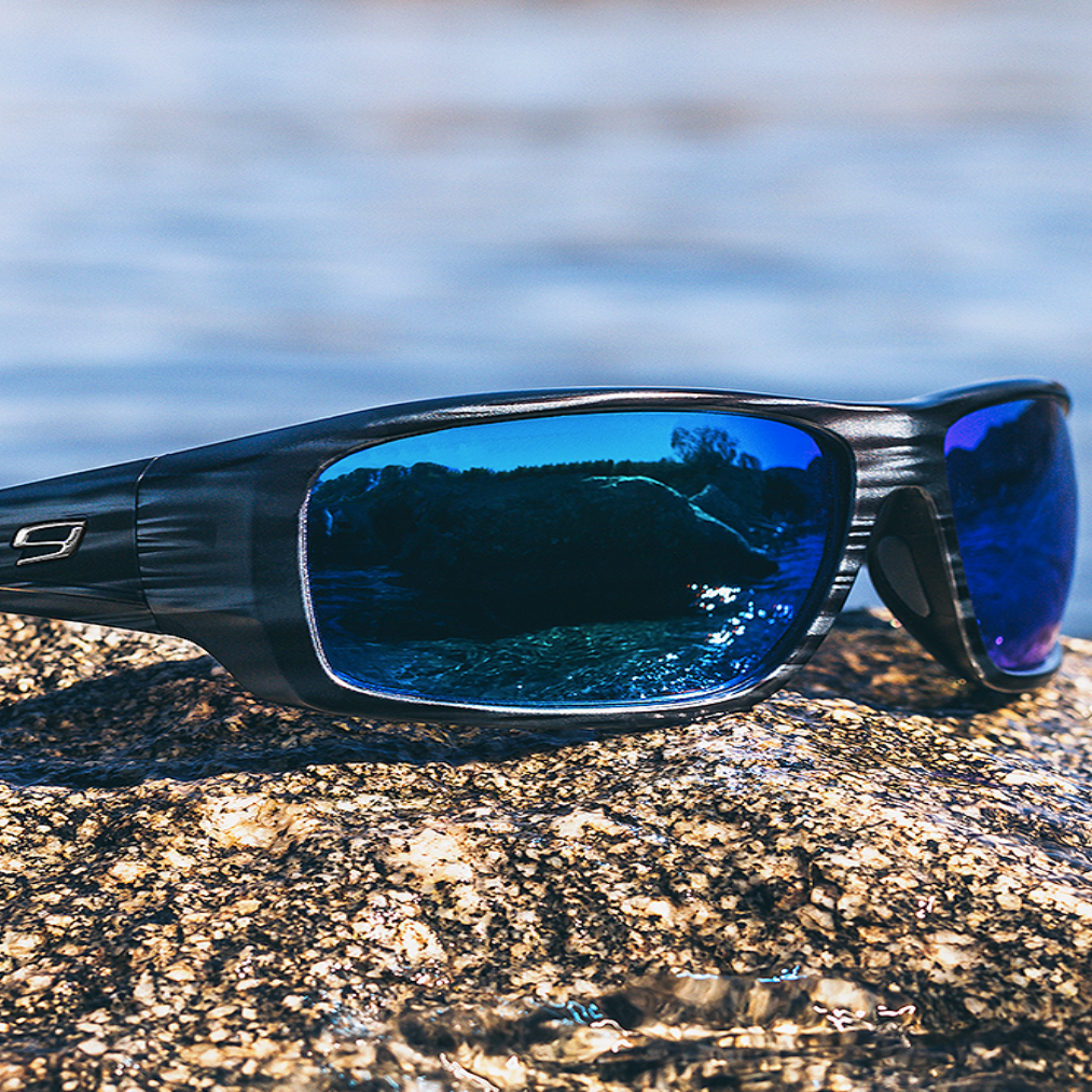 Sunglasses with blue lenses on a rock by a body of water