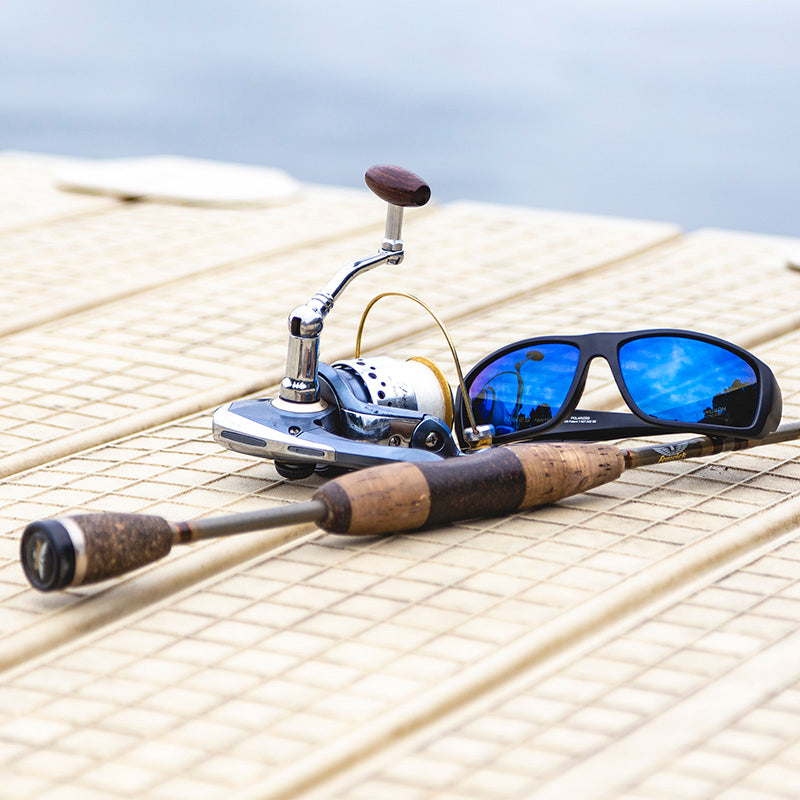 Fishing rod and reel with sunglasses on a wooden surface
