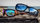 Sunglasses with reflective lenses on a wooden surface with a beach scene in the background
